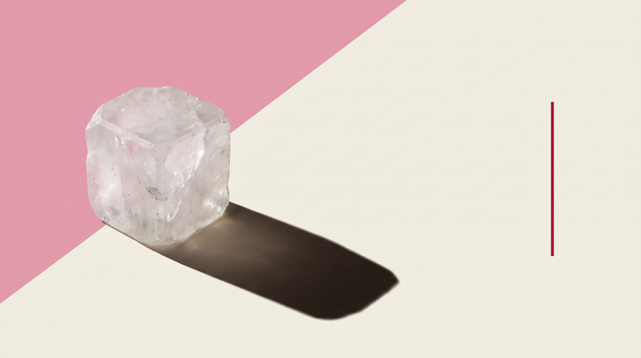 Un blocco traslucido di allume di rocca su fondo diviso in diagonale fra rosa e bianco osso