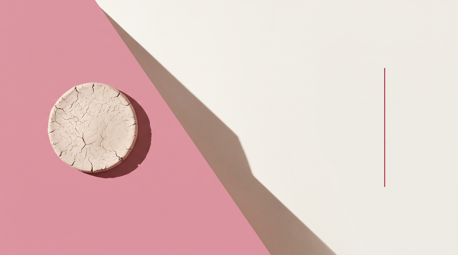 Un disco di argilla bianca essiccata e screpolata su fondo diviso in diagonale fra rosa e bianco osso