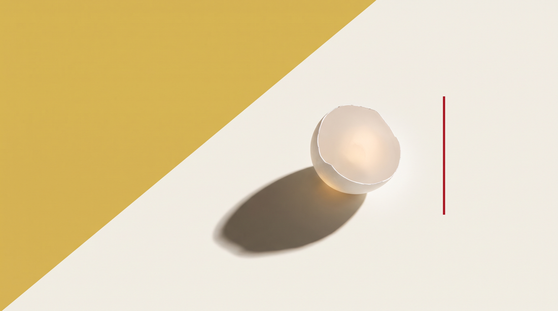 Mezzo guscio d'uovo bianco e sottilissimo attraversato dalla luce, su fondo diviso da una diagonale, metà oro e metà bianco osso