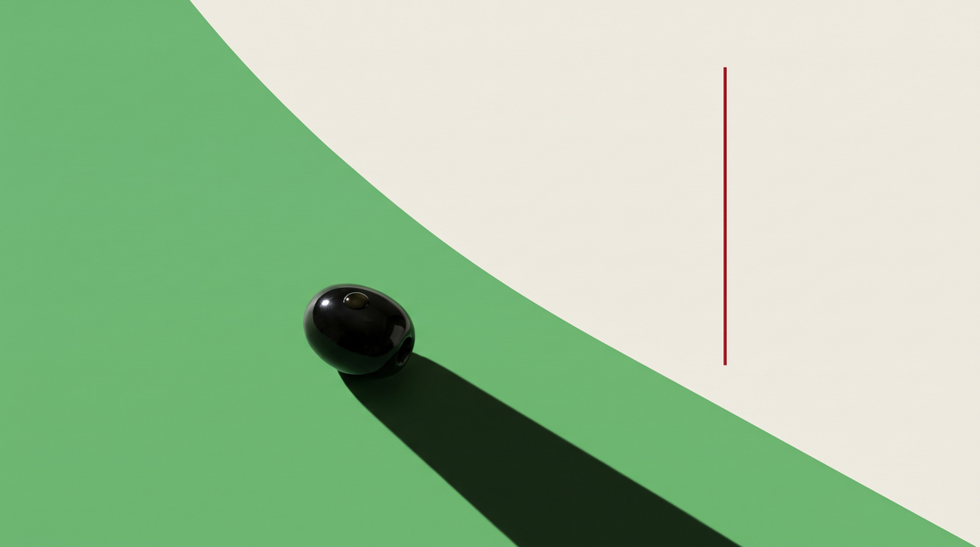 Un'oliva nera lucida con una goccia d'olio sulla buccia, su fondo diviso da una diagonale, metà verde e metà bianco osso