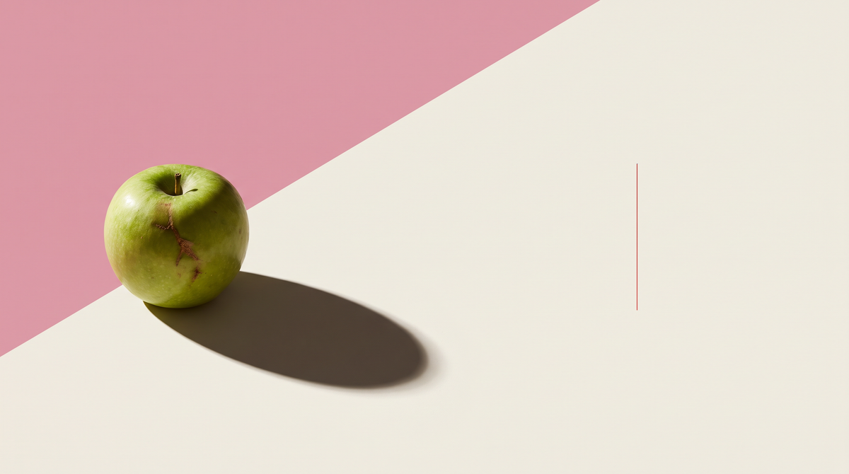 Una mela verde con una cicatrice rimarginata sulla buccia, su fondo diviso da una diagonale, metà rosa e metà bianco osso