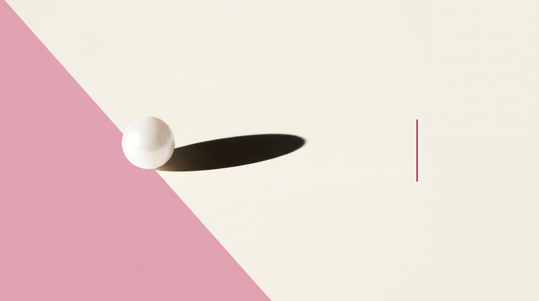 Una perla bianca opaca su fondo bianco osso attraversato da una diagonale rosa