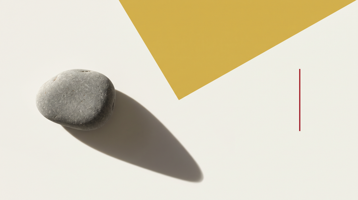 Un ciottolo grigio consumato su fondo bianco osso con campo giallo oro diagonale