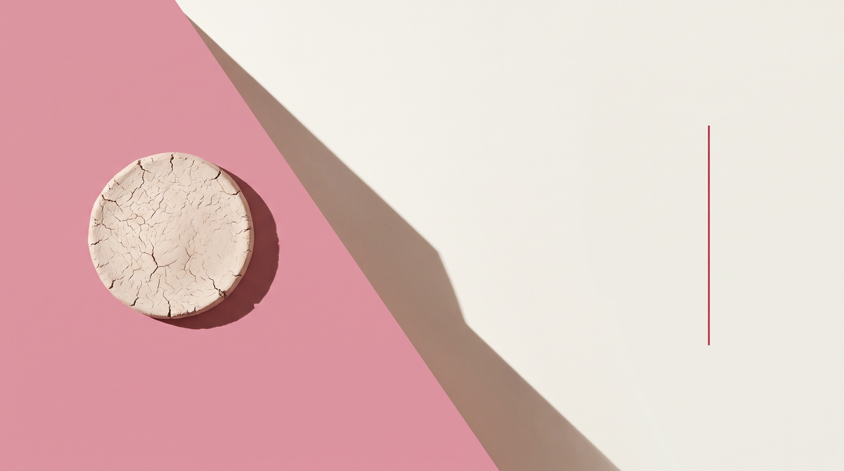 Un disco di argilla bianca essiccata e screpolata su fondo diviso in diagonale fra rosa e bianco osso
